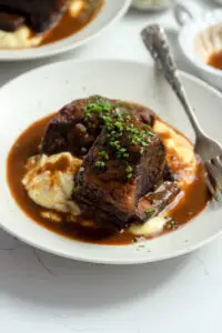 Braised Short Ribs with Red Wine Jus over polenta, garnished with crispy shallots.